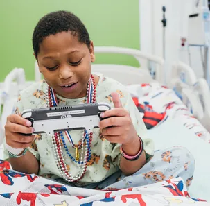 A young boy sits in a hospital bed plying a handheld gaming console